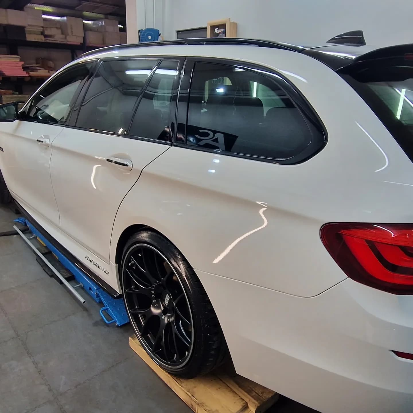 Weisser BMW 5er Touring mit schwarzen BBS-Felgen in der Werkstatt, die Flanke spiegelt die Werkstattbeleuchtung.