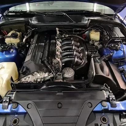 Geöffnete Motorhaube eines blauen BMW E36 M3 mit gereinigtem Motorraum und Ansaugbrücke.