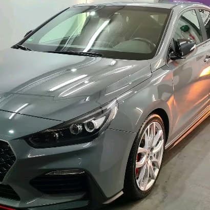 Frontpartie eines grauen Hyundai i30N Performance mit polierten Felgen und roten Bremssätteln in der Halle.